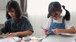© FAMILY STOCK - Asian girls doing creative DIY activity at home, developing skills and imagination in a homeschooling environment with art materials, scissors, and concentration.