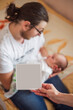 © farmuty - Father lovingly holds his newborn baby while sitting on a bed. A hand in the foreground holds a blank card, symbolizing family, love, and the beginning of a new chapter in life