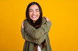 © deagreez - Happy young woman hugging herself in a casual green outfit against a vibrant yellow background