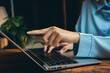 © JK_kyoto - Close-up of a female hand pointing at a laptop keyboard in a cozy workspace with soft lighting and greenery