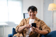 © Wasana - A man is sitting on a couch and smiling while looking at his cell phone