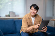 © Wasana - A man is sitting on a couch and pointing at a tablet