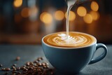 Close-up of creamy milk pouring into coffee with latte art in a blue cup, creating a warm and inviting ambiance, surrounded by scattered coffee beans.