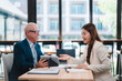 © Tj - Senior businessman showing something on tablet to young businesswoman while discussing and working together in modern office, they're smiling and looking happy