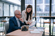© Tj - Senior businessman and young businesswoman are discussing graphs and using tablet in modern office, analyzing financial data and investment strategy