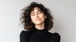 © kiimoshi - A young woman with curly hair smiles gently while embracing a moment of tranquility and self-acceptance, conveying a sense of joy and contentment in a minimalist setting.