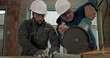 © Marco - Focused construction workers operating an angle grinder on metal, sparks flying, teamwork in action, both wearing safety helmets and protective goggles