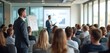 © Maryna - Businessman in suit stands in conference hall during seminar. Speaker presents financial report data on screen. Audience listens attentively to expert speech, business training. Business meeting