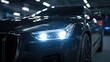 © StockHive - Sleek black car in a dimly lit garage with shining headlights.
