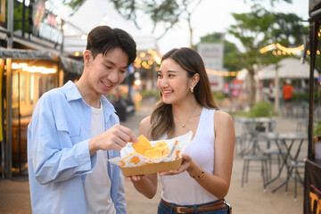 happy young friends enjoying and sharing a snack at a lively outdoor night market