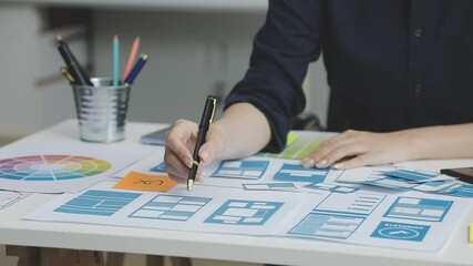UX/UI designer working on wireframes for a website and mobile app prototype, surrounded by sketches of user-flow and design tools, in concept of website and mobile application design concept.
