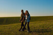 © kinomaster - Young Couple Hiking with Trekking Poles in Open Green Field