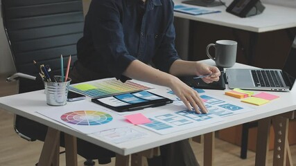 UX/UI designer working on wireframes for a website and mobile app prototype, surrounded by sketches of user-flow and design tools, in concept of website and mobile application design concept.