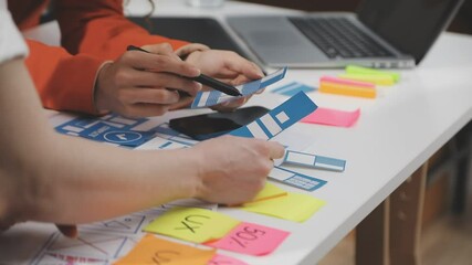 UX/UI designer working on wireframes for a website and mobile app prototype, surrounded by sketches of user-flow and design tools, in concept of website and mobile application design concept.