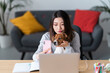 © Studio Marmellata - A young woman holds her small dog while taking a selfie with her pink smartphone. They are sitting at a desk with a laptop, likely capturing a moment together.
