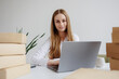 © Sandu - Woman working on laptop surrounded by packaged boxes in a modern office space during daytime