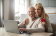 © Prostock-studio - A cheerful senior couple sits together at a table, with one partner using a laptop while the other holds a credit card, both smiling and sharing a joyful moment in their comfortable living space.
