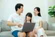 © STOCK88PHOTOGRAPHER - Asian family uses a laptop on the couch; the parents smile at each other while showing their daughter something online.