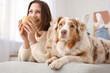 © Pixel-Shot - Happy young woman drinking tea with cute dog while lying on sofa at home
