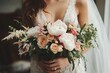 © dgete - Close-up of a bride holding a lush bouquet of white peonies, cream roses, and assorted green foliage, evoking elegance and romance