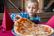 © Elena - Young Boy Enjoying a Slice of Pizza at a Restaurant