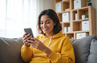 © DruZhi Art - Happy Young Woman Using Smartphone in Cozy Living Room – Smiling Person in Yellow Hoodie on Sofa for Social Media, Digital Communication, and Lifestyle Content