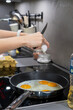 © dimetradim - Hands are shown carefully cracking a fresh egg with a knife over a hot frying pan, adding it to other eggs already cooking sunny-side up for a delicious homemade meal.
