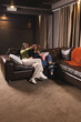 © Wavebreak Media - Sitting diverse female friends sharing popcorn boxes, pointing at screen in home theater, on couch