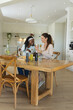 © Wavebreak Media - Clinking Diverse female friends sitting at kitchen-dining table, with wine glasses and bread