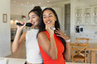 © Wavebreak Media - Standing Diverse female friends singing karaoke in modern kitchen dining area, with microphones