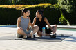 © Wavebreak Media - Sitting diverse female friends practicing yoga on pool deck, with two water bottles and smartphone