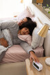 © Wavebreak Media - Sleeping Diverse male partners reaching toward alarm clock on nightstand in bedroom, with pillows