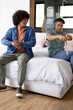 © Wavebreak Media - Stretching arms and pulling sock Diverse male friends sitting on bed in bright bedroom, with window