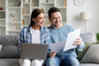 © Home-stock - Young European couple checking documents and using laptop, reading insurance agreement or property certificate, sitting on couch in cozy living room