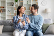 © Home-stock - Young couple using cellphone together, scrolling through apps and websites, laughing while sharing internet finds, sitting together on sofa at home