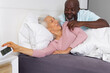 © Wavebreak Media - Smiling senior couple lying in modern bedroom on white duvet, reaching toward digital alarm clock