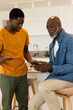 © Wavebreak Media - Showing African American father and son sitting at kitchen island and discussing smartphone