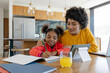 © Wavebreak Media - Guiding diverse mother and daughter writing homework at wooden island, with tablet stand, notebook