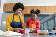 © Wavebreak Media - Diverse mother and daughter mixing ingredients at kitchen island, with red mixing bowl and whisk