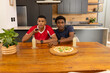 © Wavebreak Media - Diverse male friends watching TV in open-plan kitchen, with remote, pizza board and bottles