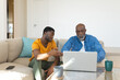 © Wavebreak Media - African American father and son sitting on couch in living room, with laptop and coffee mugs