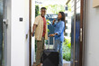 © Wavebreak Media - Pressing doorbell African American couple waiting in home entryway, with black suitcase and phones