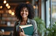 © miss irine - Smiling young woman holding books. Indoor modern interior, blurred background. Positive student, professional female with natural hair, looks confident, self assured. Education, knowledge, college,