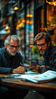 © takon - Two men discussing plans at a caf? table outdoors