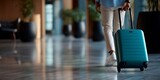 Person pushing a teal suitcase through a modern airport terminal