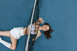 © SHOTPRIME STUDIO - Young woman in sports attire joyfully stretching on a tennis court, showcasing athleticism and vibrant energy in a dynamic outdoor setting