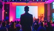 © DZIKRA  - Man faces stage, auditorium with audience. Stage lit with pink and yellow hues