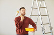 © Studio Romantic - Portrait of young handsome painter man wearing casual clothes holding paint roller and tools for renovation with confused thinking face expression. Repair home renovating house concept.