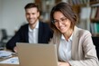 © zhao - Happy businesswoman using laptop while analyzing reports with male coworker in office. High quality