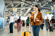 © Chanakon - Portrait of confident young businesswoman smiling at camera ready traveling business trip with holding passport with ticket boarding pass and smartphone at the international airport terminal.